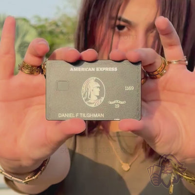 A model holds up the matte-black American Express–design Solaris metal card, showing the front then the back — blacked-out stainless steel product showcase